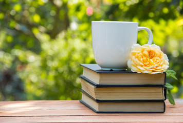 Stack of books and white cup of tea on a green natural background. Yellow rose.Tea in the garden with a book. Copy space. Stack of books.
