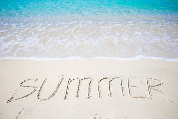 Word Summer handwritten on sandy beach with soft ocean wave on background
