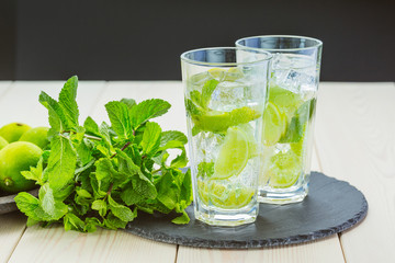 Two fresh mojitos cocktail on wooden background. Mojitos with mint leaves, lime and ice. 