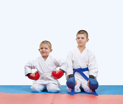 Two boys athletes in red and blue overlays sit on the mats