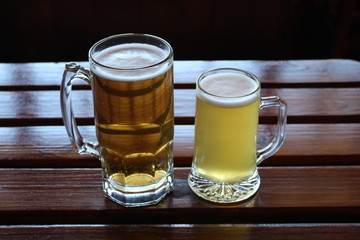 Two glasses of craft beer variety, lager and wheat beer, on a wooden table in front of a window