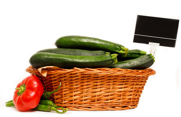 Wooden basket full of courgettes and a red capsicum and pepper on the side, for market use, isolated on whte with price tag