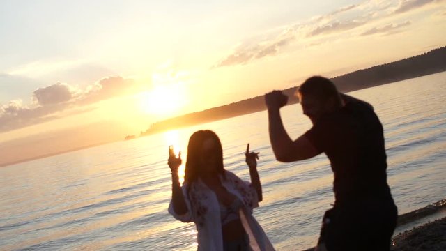 Fun man and european woman dancing on the beach in slow motion. Silhouette guy and girl on the sunset background. Free couple of people. The sun is shining slowmotion. Dance smiling on a sunny day.