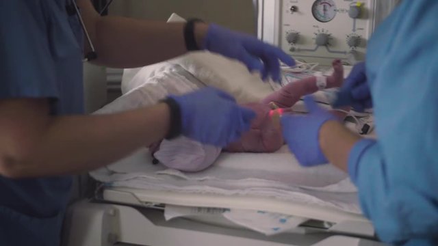 Two Nurses Attach Heart Beat Monitor to Hand of Newborn Baby Girl in Hospital