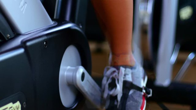Female legs and ass riding at stationary bike in the gym. Female legs
