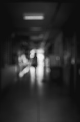 Blurred image of a people working in an hospital in walking away in a under passage to the light. Black and white image. Motion blur