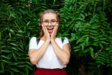 Surprised young beautiful female student in glasses posing over leaves outdoors.