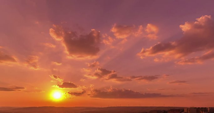 sunset scene with sun fall behind the clouds in background, time lapse shot, warm colorful sky with soft clouds ..