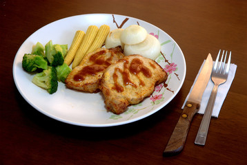 Two pieces of the pork steak topped with the brown sauce served with many kinds of vegetables and ready for eathing.