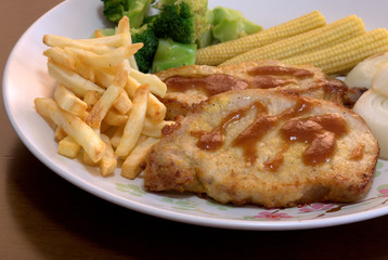 The close up shot for the pork steak topped with the brown sauce served with french fried and many kinds of vegetables.