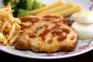 The close up shot for the pork steak topped with the brown sauce served with french fried and many kinds of vegetables.
