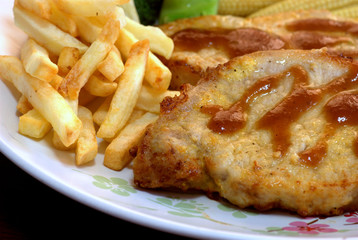 The close up shot for the pork steak topped with the brown sauce served with french fried and many kinds of vegetables.