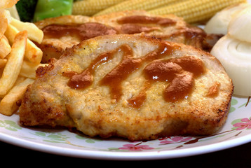 The close up shot for the pork steak topped with the brown sauce served with french fried and many kinds of vegetables.