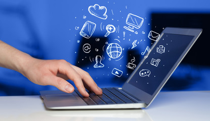 Hand writing on notebook computer with media icons