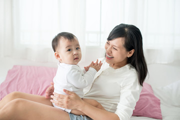 Mother and baby daughter plays, hugging, kissing at home on bed