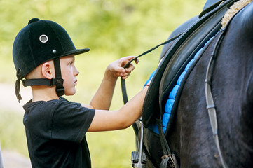 the boy saddling a horse and tighten the girth. The foreground.