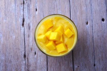 Top view of a healthy glass of mango yogurt smoothie on a wooden background.