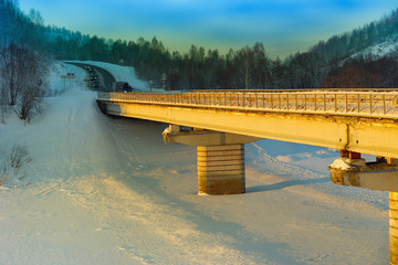 Winter landscape. Bridge lit by sun over river covered snow. Sunset. Kemerovo region. Siberia. Russia.