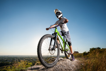 Fototapeta na wymiar Cyclist in helmet and glasses stay on the mountain bicycle at the hill under blue sky against blue sky and looking into the distance. Wide angle view