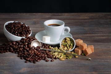 Coffee beans, cardamom seeds, cane sugar and espresso cup on a wooden table. Special light. Toned image.
