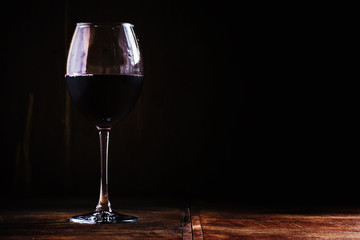Chilled dry red wine in the glass. Dark vintage wood background.