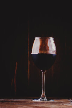 Chilled dry red wine in the glass. Dark vintage wood background.