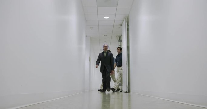 Group of four business men led by creative executive with purple hair walk down a plain white corridor.  Wide shot, recorded from static camera at dramatic low angle in slow motion at 60fps.