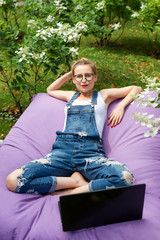 Obraz premium Freelancer working in the garden. Writing, surfing in the internet. Young woman relaxing and having fun in park area. Distance education, freelance concept.