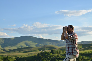 Man is using binoculars to observe wonderful summer scenic landscape
