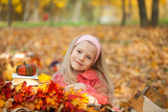 Young girl in autumn park with books, bouquet and little pumpkin