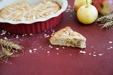 Homemade apple pie in the baking dish with apples and ears of wheat on the burgundy background