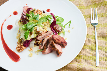 A healthy Breakfast consisting of a salad with duck breast, daikon, grapes and couscous served on a white plate