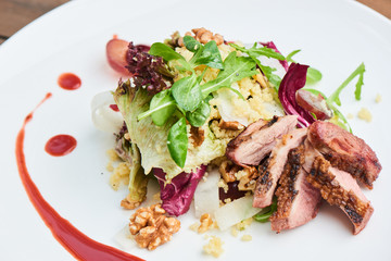Salad of duck breast, daikon, grapes and couscous served on a white plate