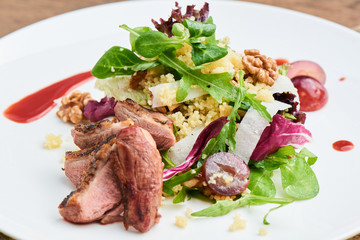 Salad of duck breast, daikon, grapes and couscous served on a white plate