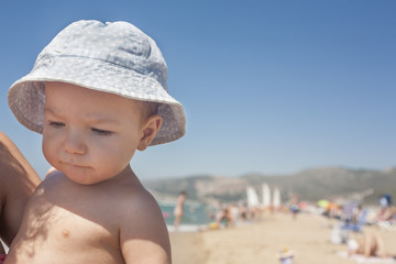 Mother holding baby boy with blue hat on the beach