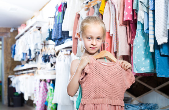 Little girl holding dress in hands in children clothes boutique