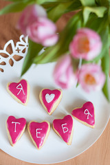 Homemade glazed cookies with "I love you" in Russian and bouquet of pink tulips, view from above