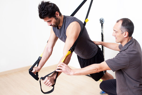Personal trainer helping with suspension stretching exercise - Powered by Adobe