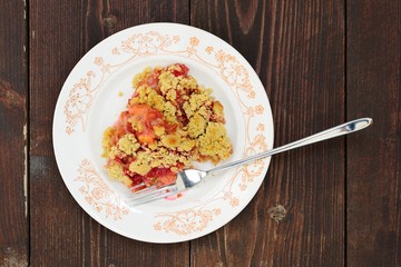 Plum crumble in white plate on dark wooden background