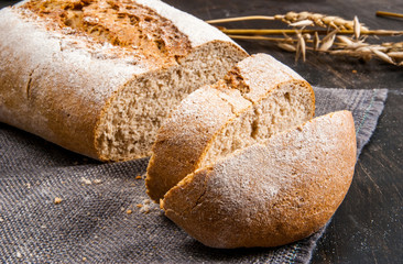 Fragrant fresh-baked rye bread on a black wooden table. Bread is sliced. Spikelets of wheat and rye close. Rustic Style. Close view