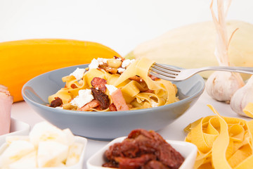 Pappardelle with zucchini, ham, dried tomatoes, garlic and feta cheese being eaten with a fork