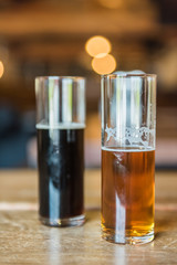 Two small glasses of beer for tasting in rustic room with pale ale and dark stout
