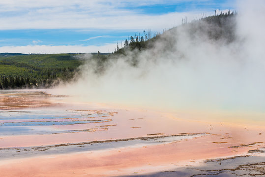 Rising blue steam and mist from Grand Prismatic hot spring in Midway Geyser basin at Yellowstone National Park with red bacterial patterns