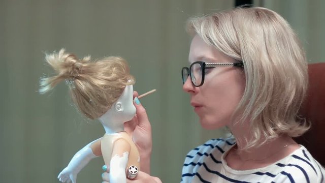 Young woman is painting a doll making her scary