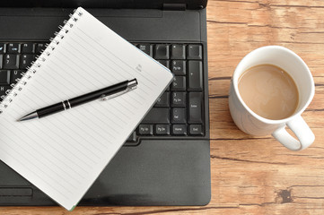 Laptop with a notebook and pen and a mug of coffee