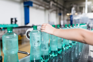 Water bottling line for processing and bottling pure mineral carbonated water into bottles. Female hand checking out water bottles. Selective focus.