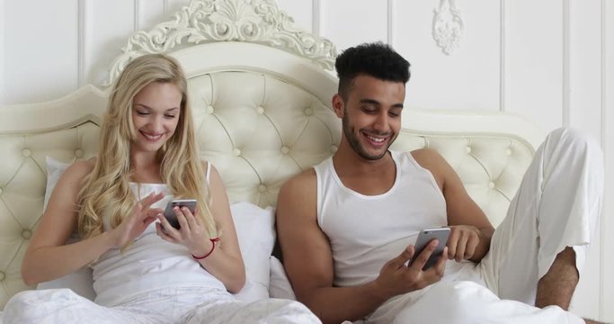 Couple lying bed using smart phone, mix race man woman smile morning bedroom