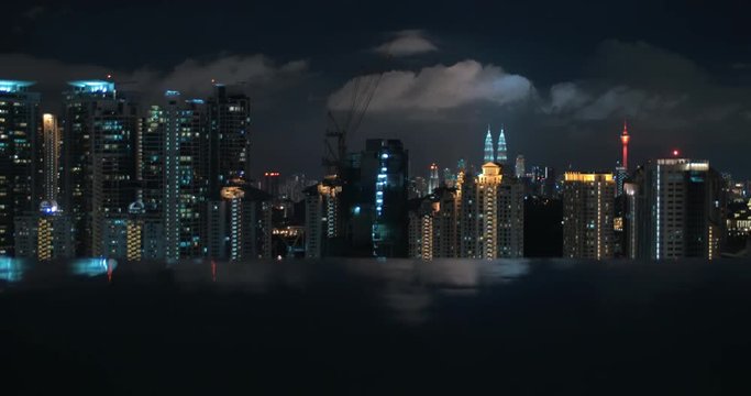 Dark water of rooftop swimming pool and night Kuala Lumpur cityscape with illuminated buildings. Shot with changing focus