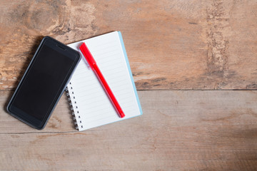 Smart phone with notebook on wooden table background with copy space