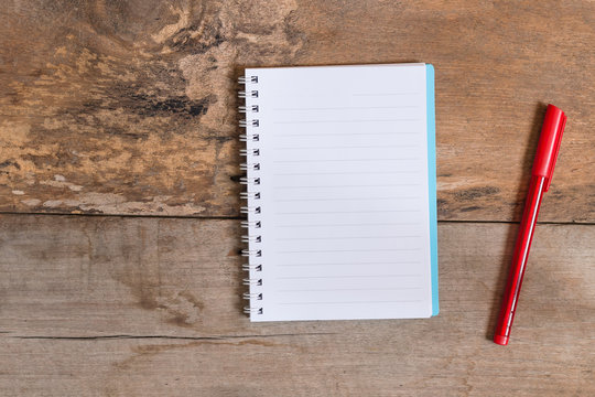 Notebook with a red pen on wood background.